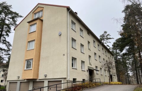 Gult trevåningshus med garageinfart i källarplan